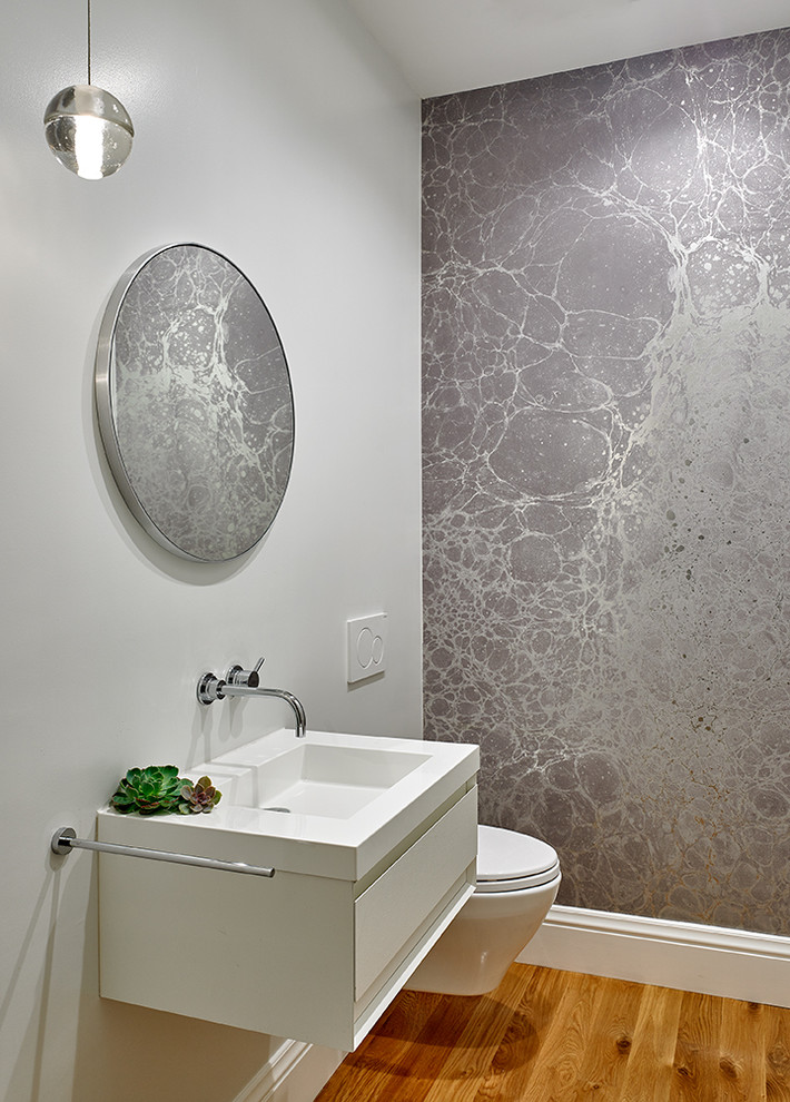 Photo of a contemporary powder room in San Francisco with flat-panel cabinets, white cabinets, a wall-mount toilet, grey walls, medium hardwood floors, a console sink, brown floor and white benchtops.