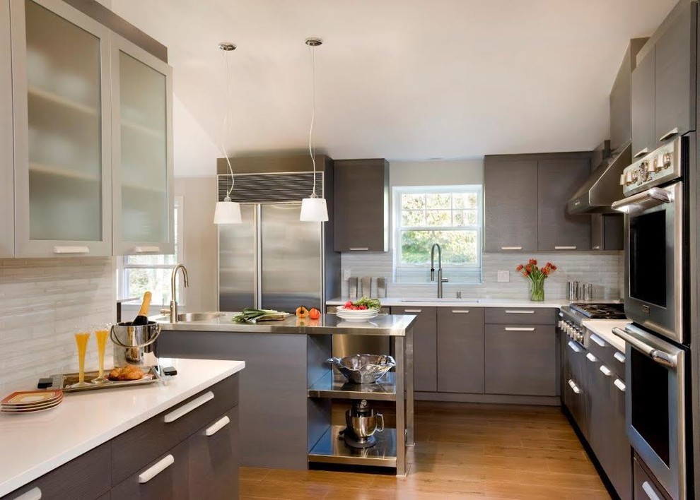 Design ideas for a large modern u-shaped separate kitchen in Boston with an integrated sink, flat-panel cabinets, grey cabinets, stainless steel benchtops, white splashback, ceramic splashback, stainless steel appliances, medium hardwood floors and with island.
