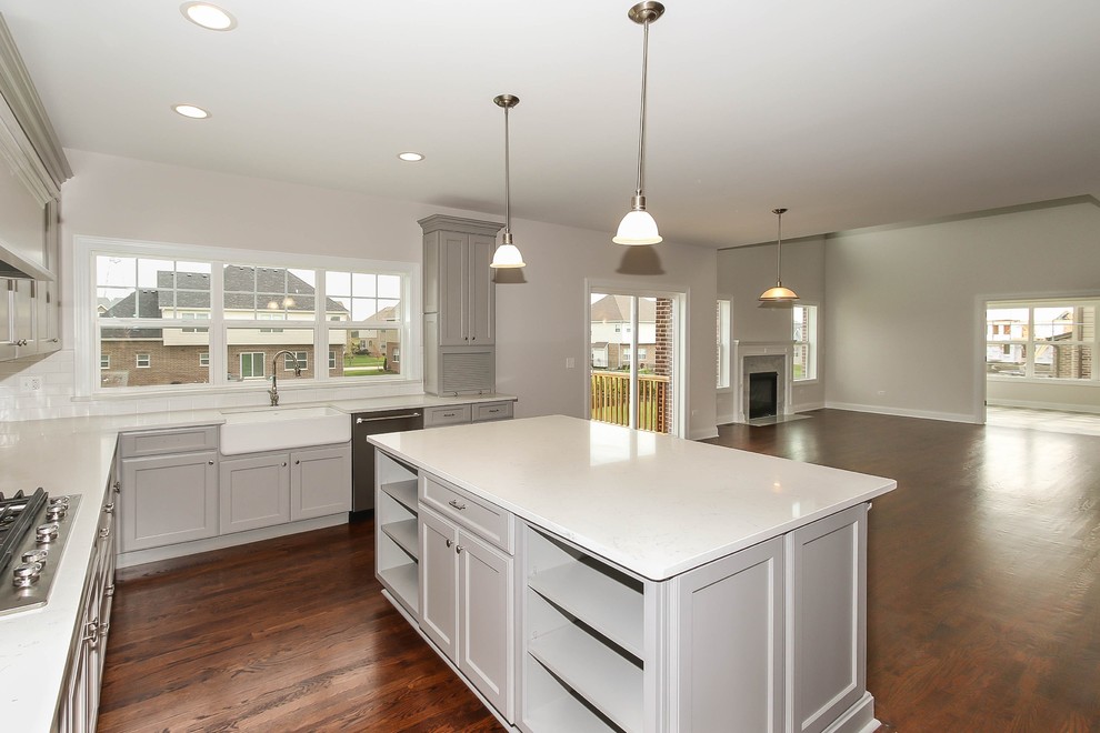 Photo of a large transitional u-shaped open plan kitchen in Chicago with a farmhouse sink, shaker cabinets, grey cabinets, quartz benchtops, white splashback, porcelain splashback, stainless steel appliances, medium hardwood floors, with island and brown floor.