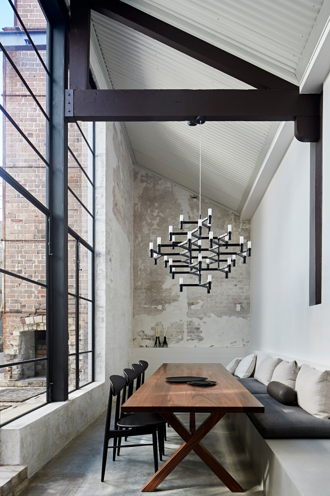 Photo of an industrial dining room in Sydney with white walls, concrete floors, no fireplace, grey floor, vaulted and brick walls.