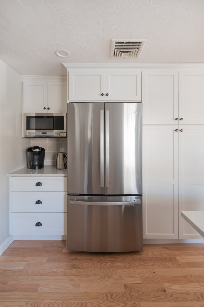 Inspiration for a large transitional galley light wood floor and brown floor eat-in kitchen remodel in Boston with an undermount sink, shaker cabinets, white cabinets, quartz countertops, beige backsplash, ceramic backsplash, stainless steel appliances, an island and white countertops
