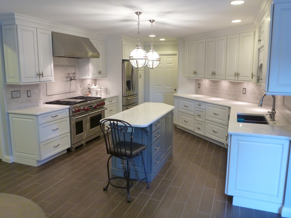Large transitional u-shaped laminate floor and brown floor open concept kitchen photo with an undermount sink, raised-panel cabinets, white cabinets, quartz countertops, beige backsplash, subway tile backsplash, stainless steel appliances and an island