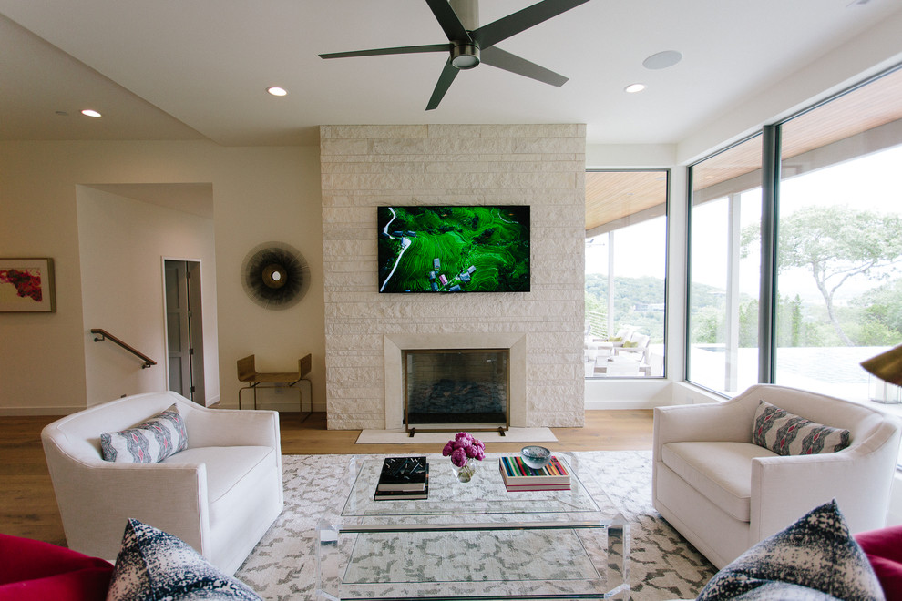 Mid-sized modern formal open concept living room in Austin with white walls, light hardwood floors, a standard fireplace, a stone fireplace surround, a wall-mounted tv and brown floor.