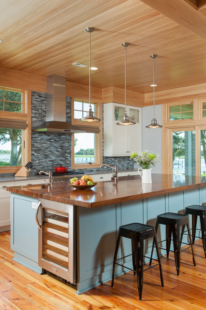 Mid-sized beach style galley open plan kitchen in Other with a farmhouse sink, white cabinets, blue splashback, light hardwood floors and with island.