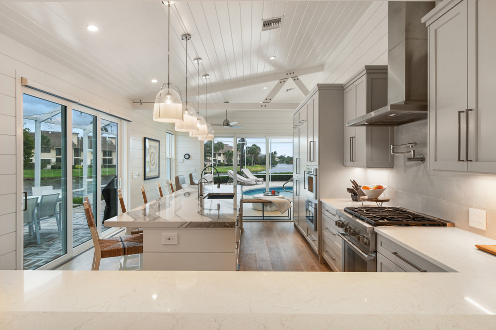 Mid-sized beach style l-shaped open plan kitchen in Other with an undermount sink, grey cabinets, quartz benchtops, stainless steel appliances, light hardwood floors, with island, grey floor and white benchtop.