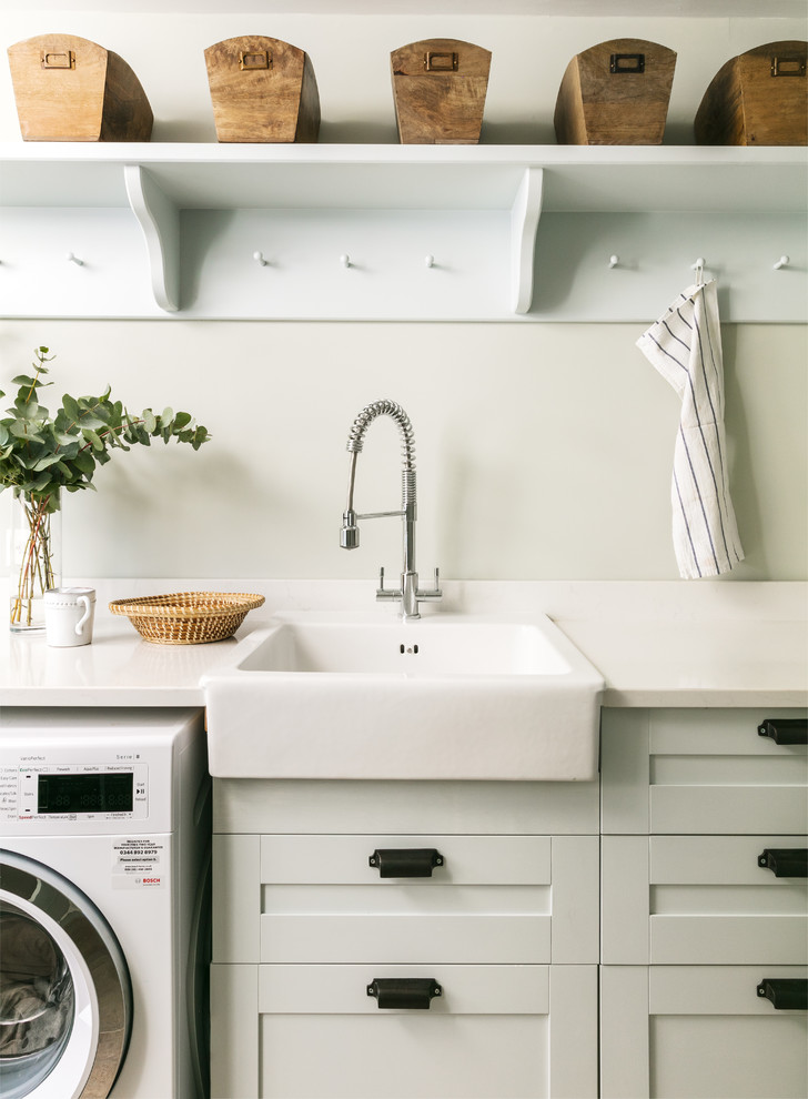 Inspiration for a beach style laundry room in London with a farmhouse sink, shaker cabinets, grey cabinets, grey walls and white benchtop.