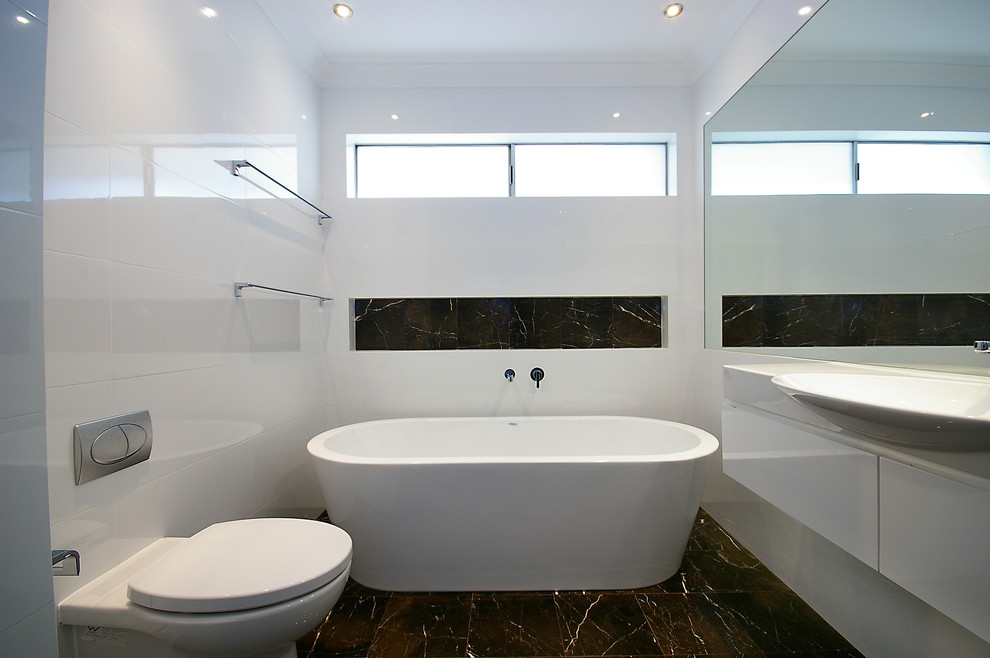 This is an example of a mid-sized modern master bathroom in Sydney with a vessel sink, recessed-panel cabinets, white cabinets, laminate benchtops, a freestanding tub, an open shower, a wall-mount toilet, white tile, porcelain tile, white walls and marble floors.