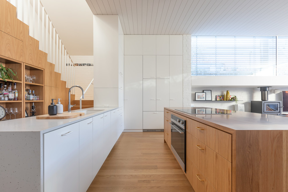 Inspiration for a small contemporary galley kitchen in Melbourne with an undermount sink, recessed-panel cabinets, white cabinets, black appliances, light hardwood floors, multiple islands, brown floor and multi-coloured benchtop.