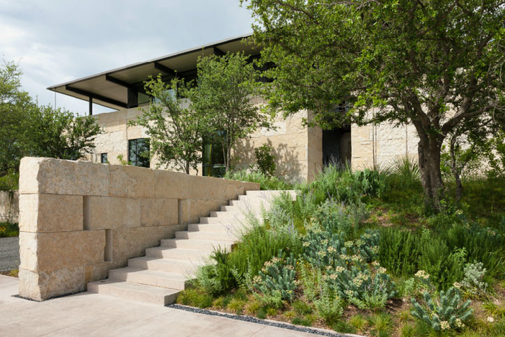 Inspiration for a large modern sloped full sun garden in Austin with a retaining wall and concrete pavers.