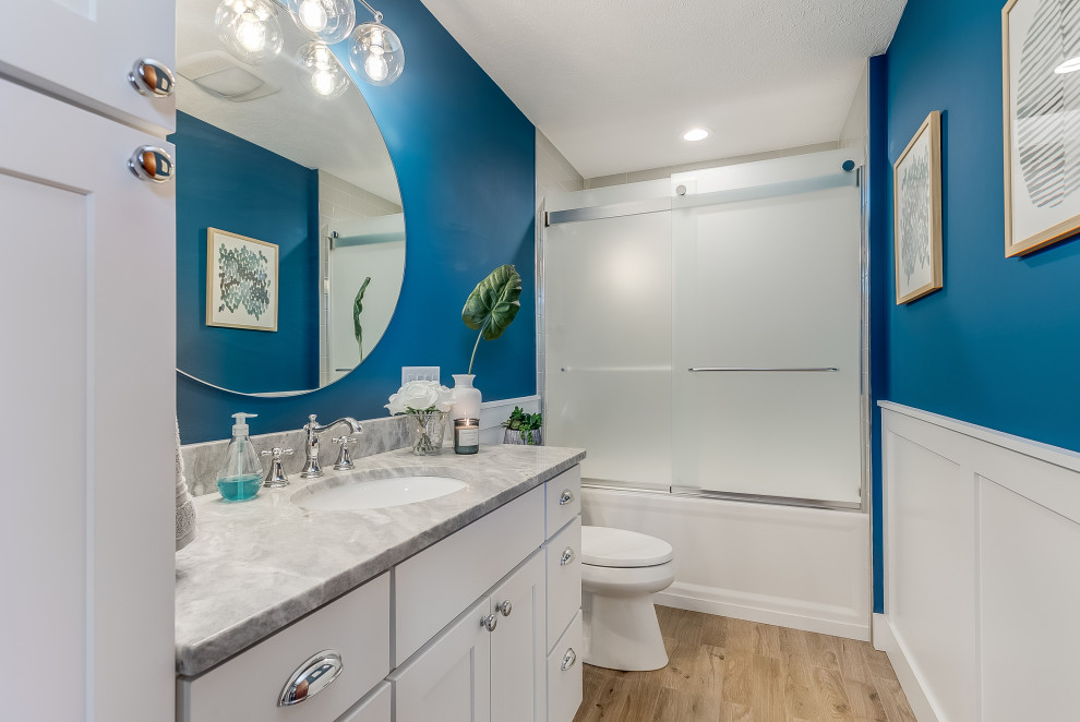 Alcove shower - mid-sized transitional 3/4 beige floor, single-sink and wainscoting alcove shower idea with shaker cabinets, white cabinets, blue walls, an undermount sink, gray countertops and a built-in vanity