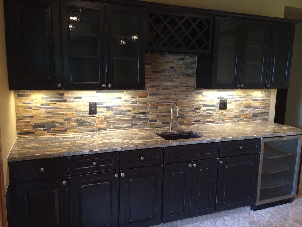 This is an example of a mid-sized transitional single-wall wet bar in Denver with an undermount sink, glass-front cabinets, dark wood cabinets, granite benchtops, multi-coloured splashback, stone tile splashback and carpet.