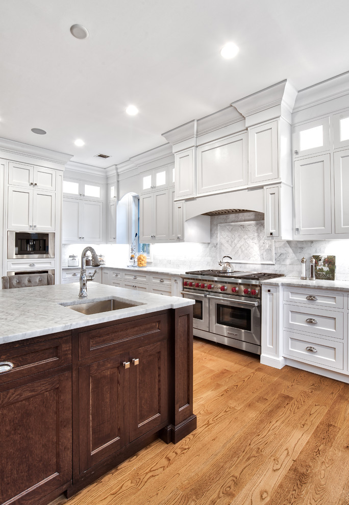 Example of a huge transitional u-shaped light wood floor and brown floor open concept kitchen design in New York with a farmhouse sink, shaker cabinets, white cabinets, quartzite countertops, white backsplash, porcelain backsplash, paneled appliances, an island and multicolored countertops