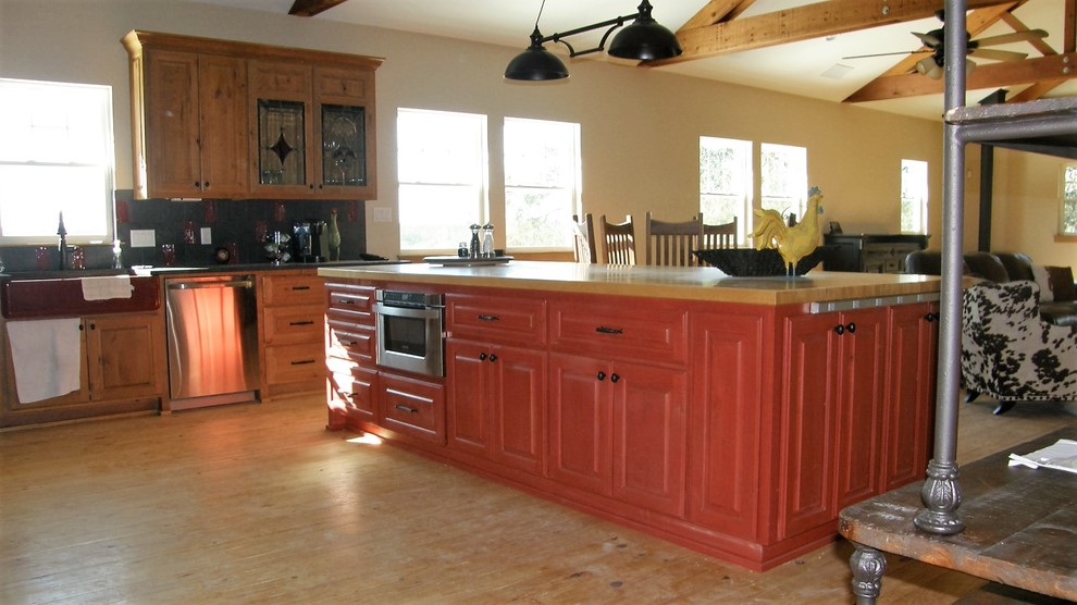 This is an example of a mid-sized country u-shaped eat-in kitchen in Austin with a farmhouse sink, raised-panel cabinets, wood benchtops, stainless steel appliances, with island, red cabinets, grey splashback, engineered quartz splashback, light hardwood floors, beige floor and beige benchtop.