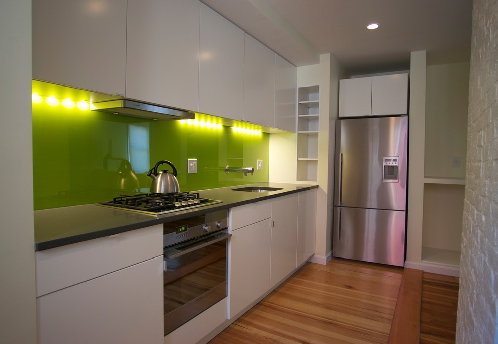 This is an example of a modern l-shaped eat-in kitchen in Boston with an undermount sink, flat-panel cabinets, white cabinets, quartz benchtops, green splashback, glass sheet splashback and stainless steel appliances.