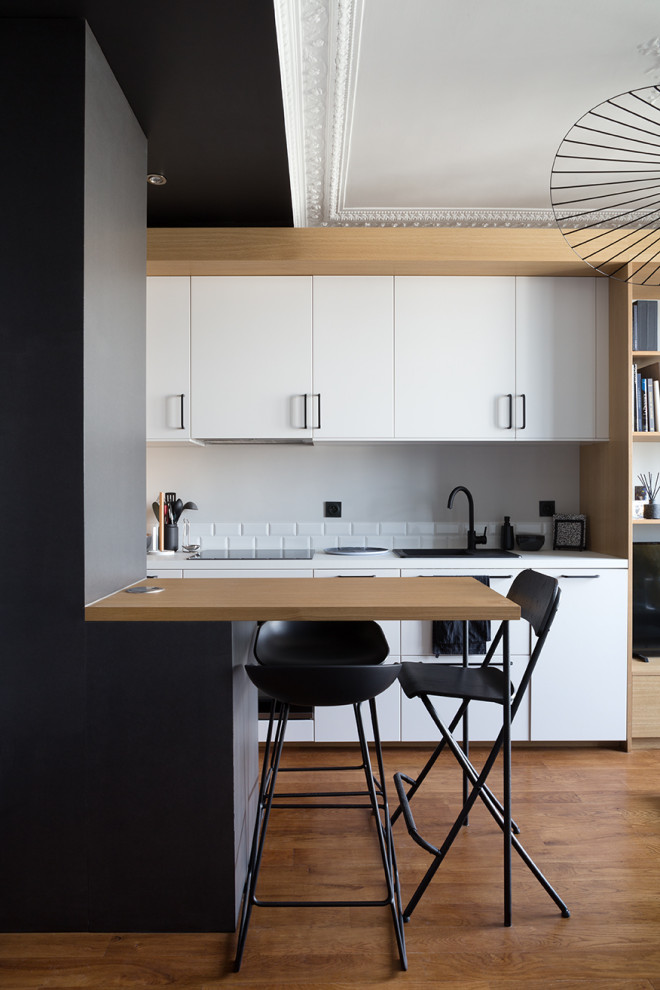 Design ideas for a small scandinavian kitchen in Paris with a drop-in sink, flat-panel cabinets, white cabinets, white splashback, subway tile splashback, medium hardwood floors, a peninsula and white benchtop.