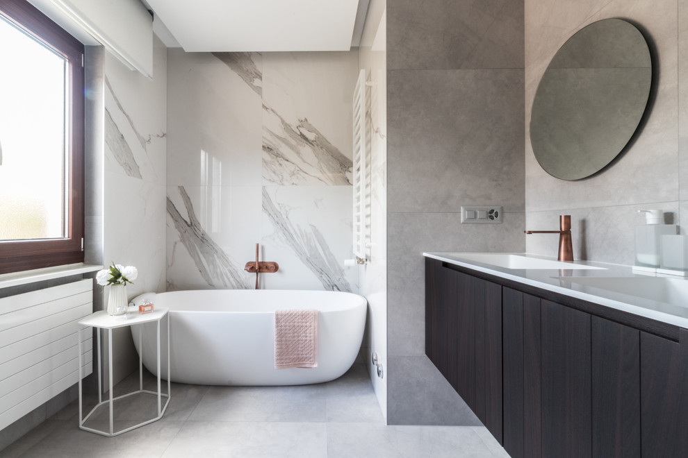 Mid-sized contemporary master bathroom in Other with dark wood cabinets, a wall-mount toilet, gray tile, porcelain tile, grey walls, porcelain floors, an integrated sink, solid surface benchtops, grey floor, white benchtops, flat-panel cabinets and a freestanding tub.