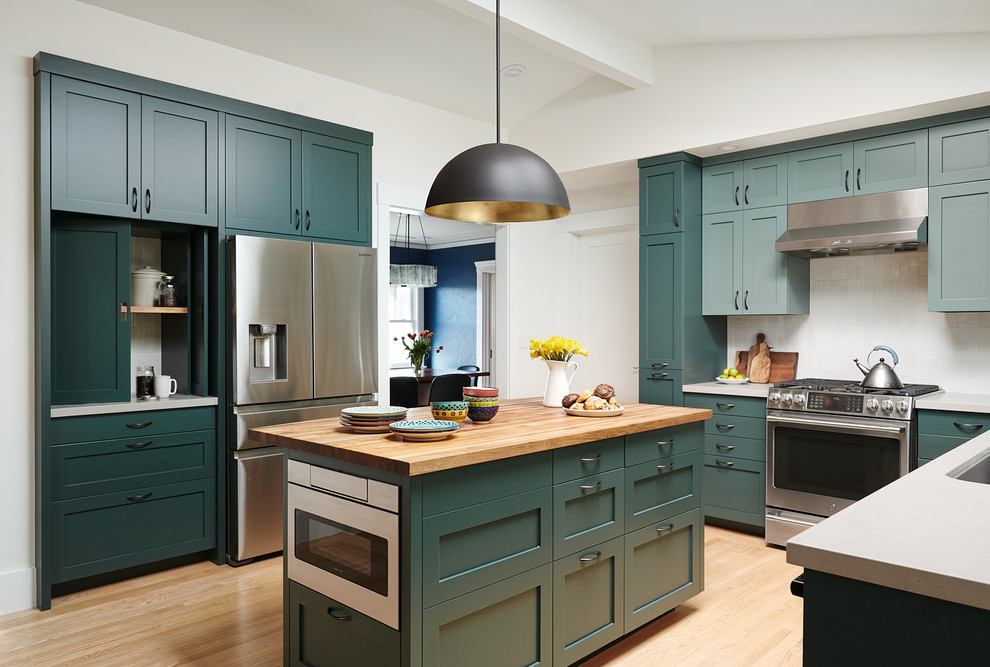 This is an example of a transitional u-shaped separate kitchen in San Francisco with shaker cabinets, green cabinets, white splashback, stainless steel appliances, light hardwood floors, with island, beige floor, grey benchtop and vaulted.