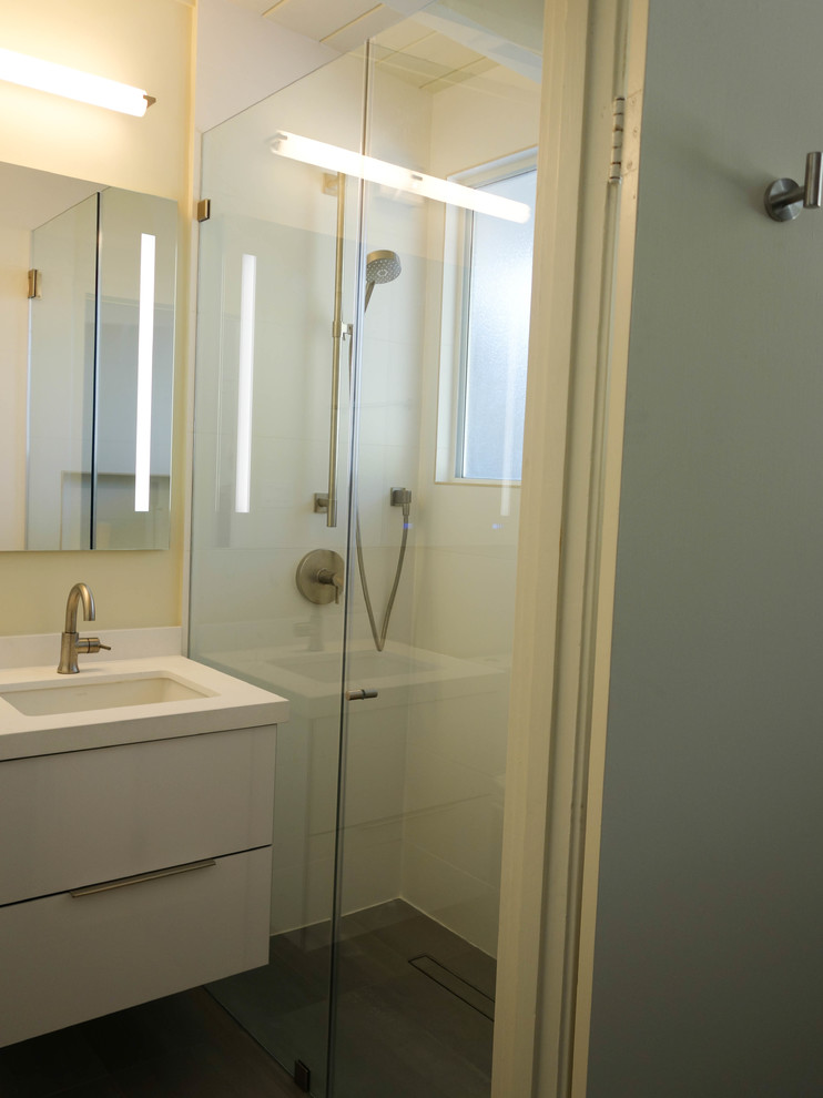 Mid-sized midcentury 3/4 bathroom in San Francisco with flat-panel cabinets, white cabinets, an alcove shower, a two-piece toilet, white tile, porcelain tile, white walls, concrete floors, an undermount sink, engineered quartz benchtops, grey floor, a hinged shower door and white benchtops.