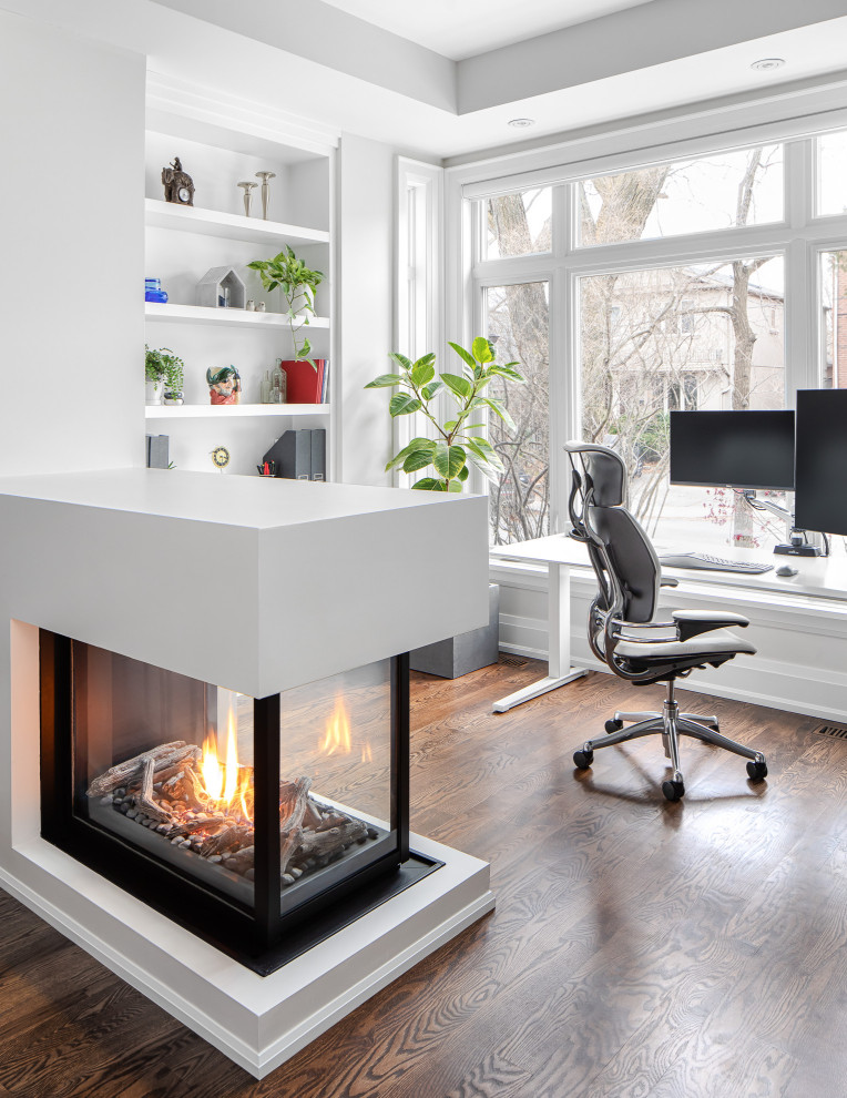 Photo of a mid-sized transitional home office in Toronto with white walls, a two-sided fireplace, a plaster fireplace surround, planked wall panelling, a library and a freestanding desk.