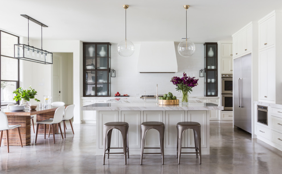 This is an example of an expansive transitional l-shaped eat-in kitchen in Houston with an undermount sink, shaker cabinets, white cabinets, marble benchtops, white splashback, porcelain splashback, stainless steel appliances, concrete floors, multiple islands, grey floor and white benchtop.