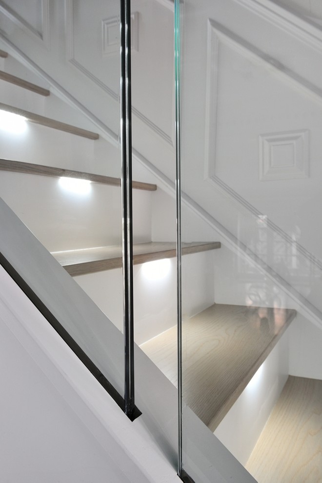 Large contemporary wood curved staircase in London with glass risers and glass railing.