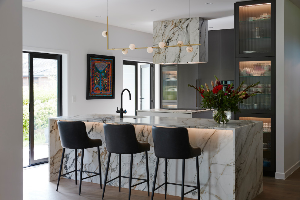 Moderne Küche in U-Form mit Unterbauwaschbecken, flächenbündigen Schrankfronten, grauen Schränken, Elektrogeräten mit Frontblende, braunem Holzboden, zwei Kücheninseln, braunem Boden und weißer Arbeitsplatte in Auckland