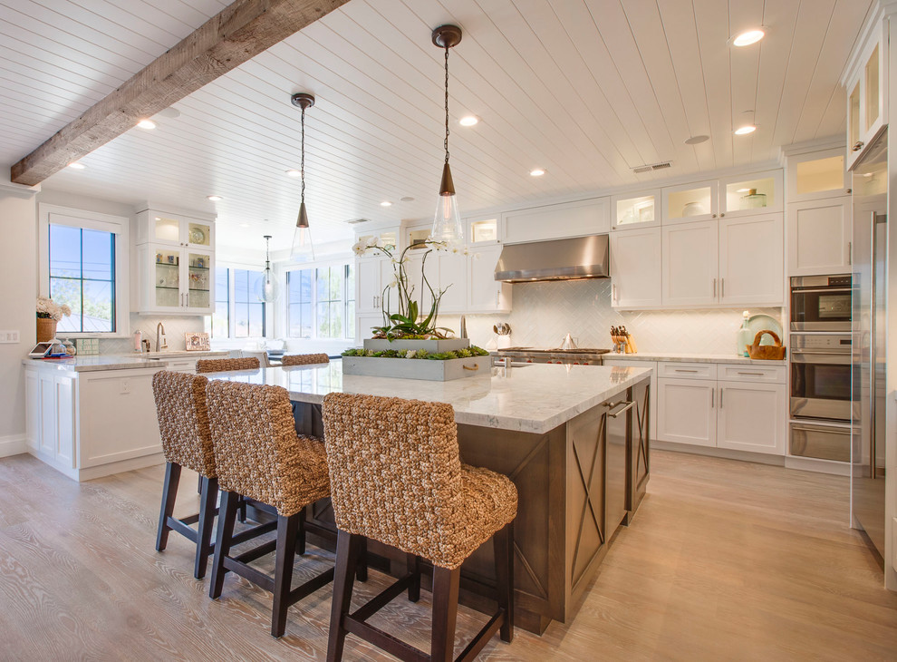 Design ideas for a beach style u-shaped kitchen in Los Angeles with an undermount sink, shaker cabinets, white cabinets, white splashback, stainless steel appliances, medium hardwood floors, with island and brown floor.