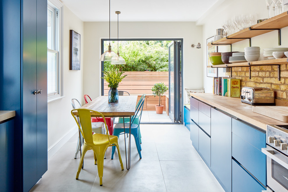 Inspiration for an eclectic eat-in kitchen in London with flat-panel cabinets, blue cabinets, wood benchtops, beige splashback, stainless steel appliances and no island.