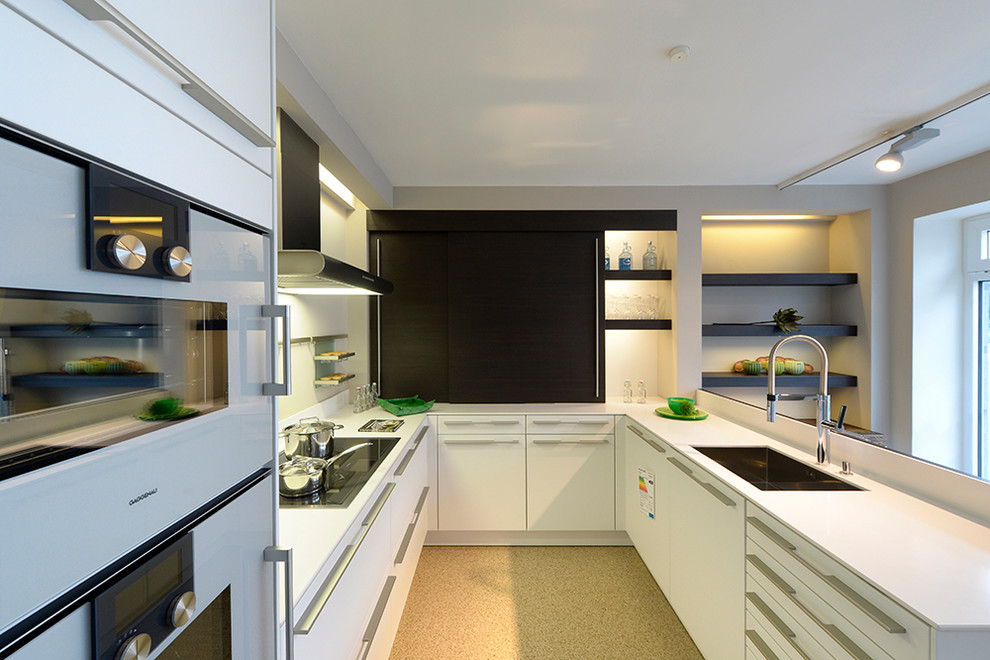 Mid-sized contemporary u-shaped separate kitchen in Other with an integrated sink, flat-panel cabinets, white cabinets, solid surface benchtops, a peninsula, white splashback, white appliances and beige floor.