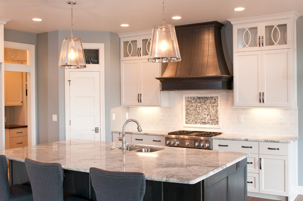 Large trendy l-shaped medium tone wood floor eat-in kitchen photo in Milwaukee with an undermount sink, recessed-panel cabinets, white cabinets, granite countertops, white backsplash, ceramic backsplash, stainless steel appliances and an island