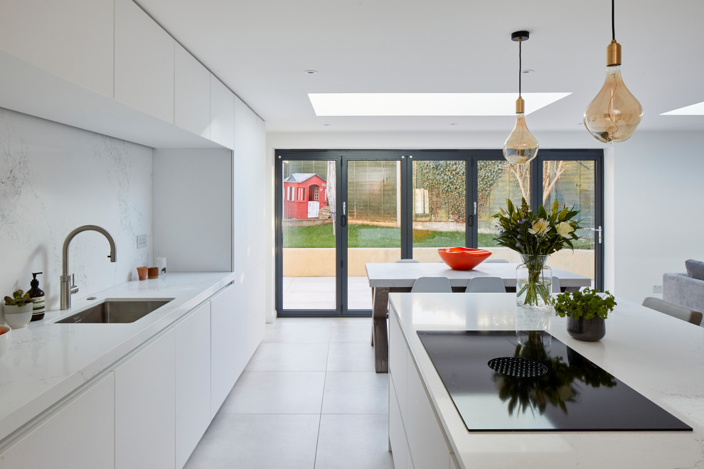 This is an example of a large contemporary single-wall open plan kitchen in Kent with an undermount sink, flat-panel cabinets, white cabinets, quartz benchtops, white splashback, engineered quartz splashback, stainless steel appliances, ceramic floors, with island and white benchtop.