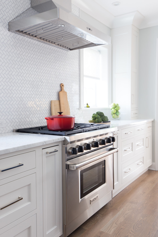 This is an example of a mid-sized transitional l-shaped eat-in kitchen in New York with an undermount sink, shaker cabinets, white cabinets, marble benchtops, white splashback, stone tile splashback, stainless steel appliances, medium hardwood floors and with island.