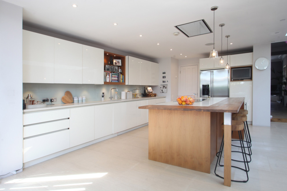 Inspiration for a mid-sized contemporary l-shaped eat-in kitchen in London with a drop-in sink, flat-panel cabinets, white cabinets, quartzite benchtops, blue splashback, granite splashback, white appliances, ceramic floors, with island, beige floor, white benchtop and recessed.