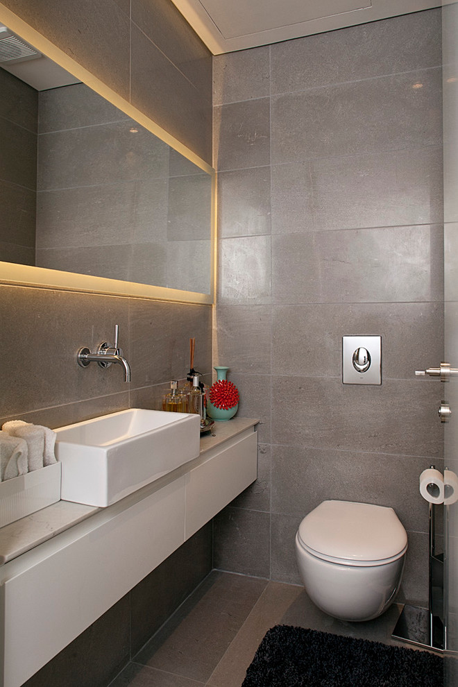 Mid-sized contemporary powder room in Tel Aviv with flat-panel cabinets, white cabinets, a wall-mount toilet, gray tile, limestone floors, limestone and a vessel sink.