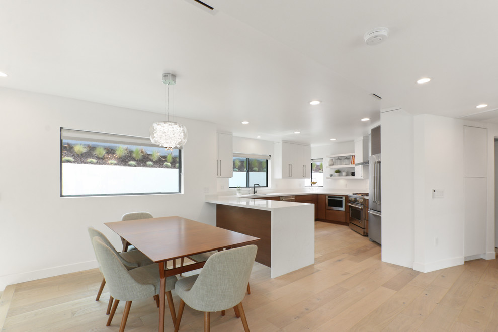 This is an example of a mid-sized contemporary u-shaped kitchen in Los Angeles with an undermount sink, flat-panel cabinets, quartz benchtops, white splashback, stainless steel appliances, with island, brown floor and white benchtop.
