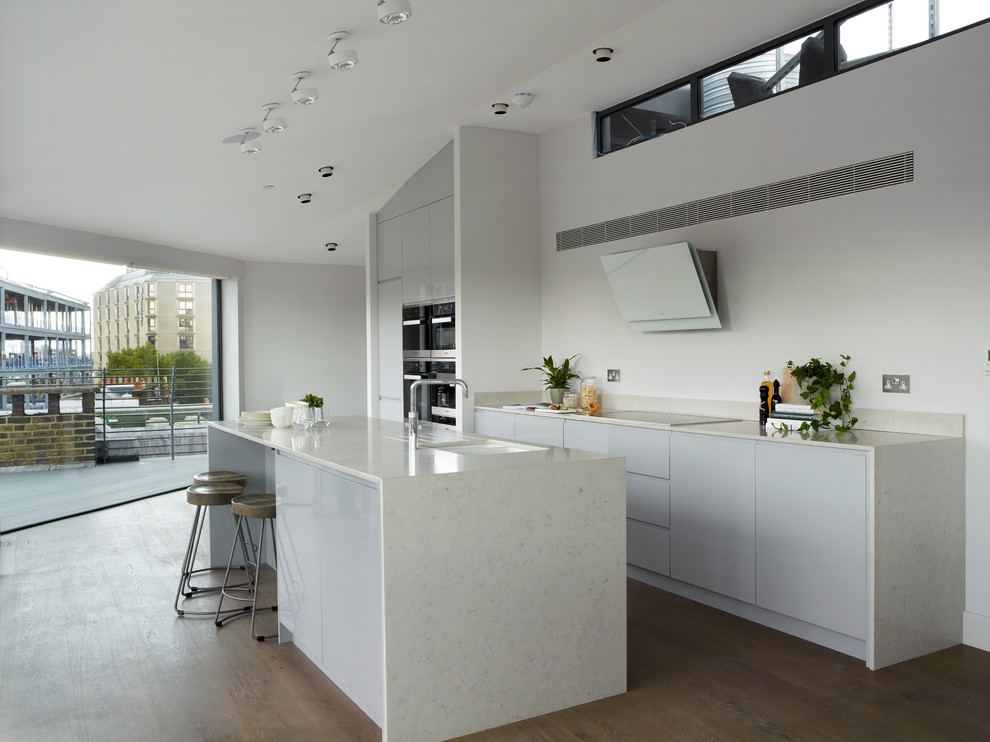 Photo of a large contemporary l-shaped eat-in kitchen in London with flat-panel cabinets, grey cabinets, solid surface benchtops, yellow splashback, no island and white benchtop.