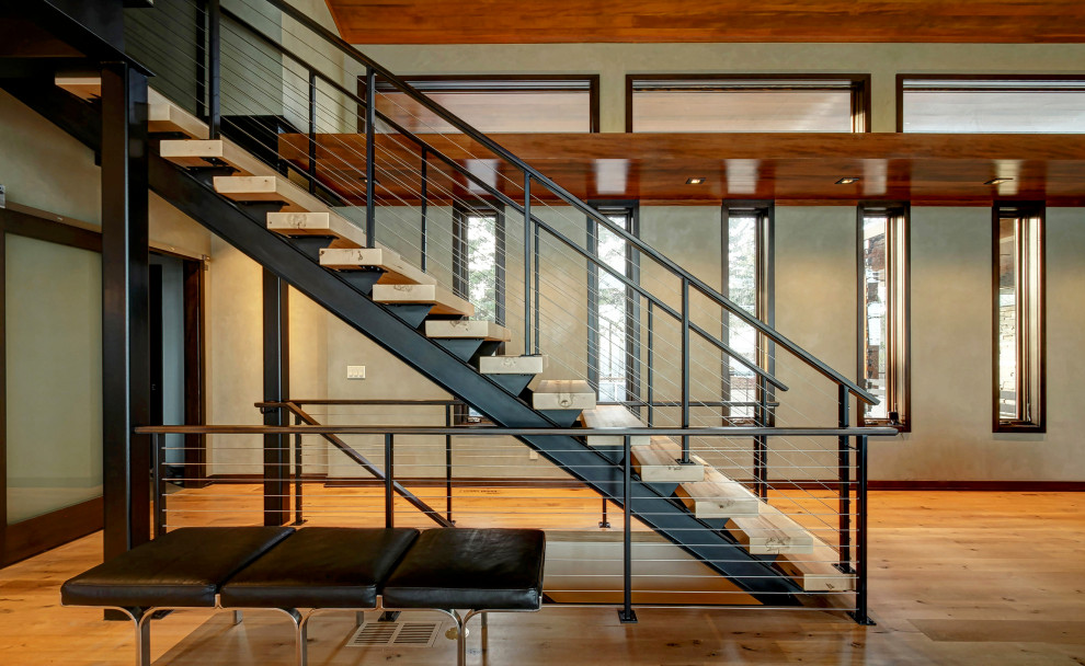 Стильный дизайн: большая лестница на больцах в стиле модернизм с деревянными ступенями и перилами из тросов без подступенок - последний тренд