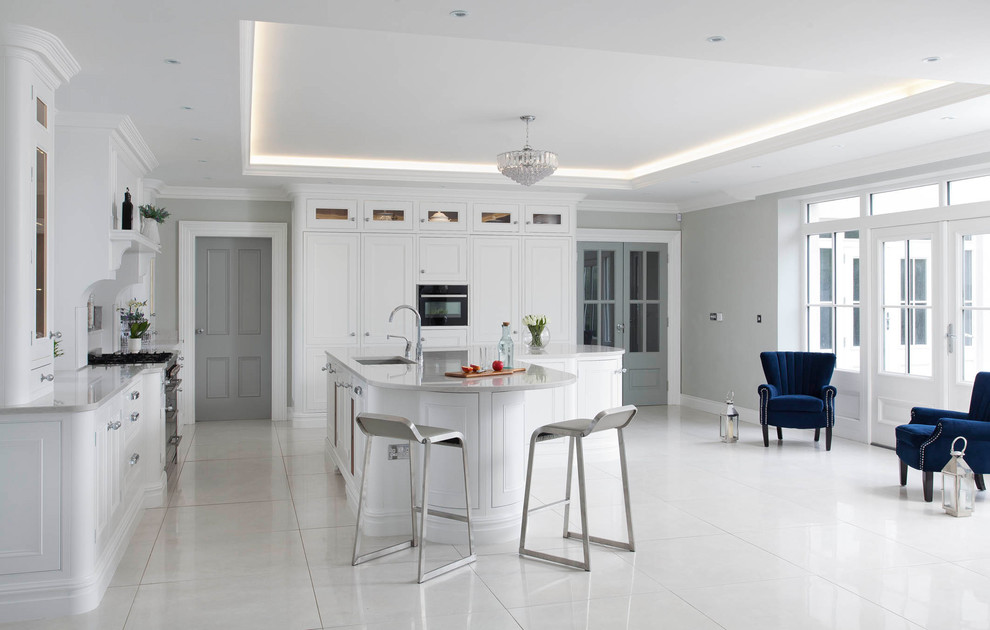 This is an example of a large transitional l-shaped open plan kitchen in Belfast with an undermount sink, beaded inset cabinets, white cabinets, quartzite benchtops, grey splashback, stone slab splashback, stainless steel appliances, porcelain floors, with island and grey floor.