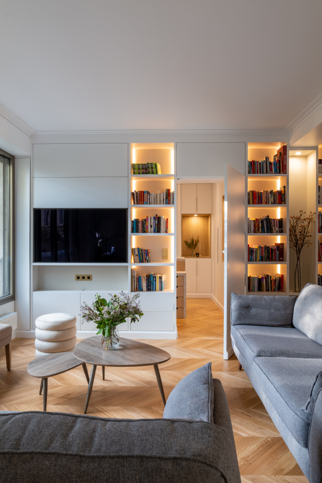 Aménagement d'un grand salon beige et blanc contemporain ouvert avec une bibliothèque ou un coin lecture, un mur blanc, parquet clair, aucune cheminée, un téléviseur encastré, un sol marron et éclairage.