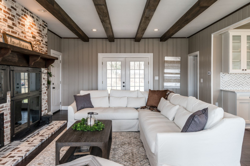Photo of a country open concept family room in Other with grey walls, dark hardwood floors, a standard fireplace, a brick fireplace surround, no tv, brown floor, exposed beam and panelled walls.