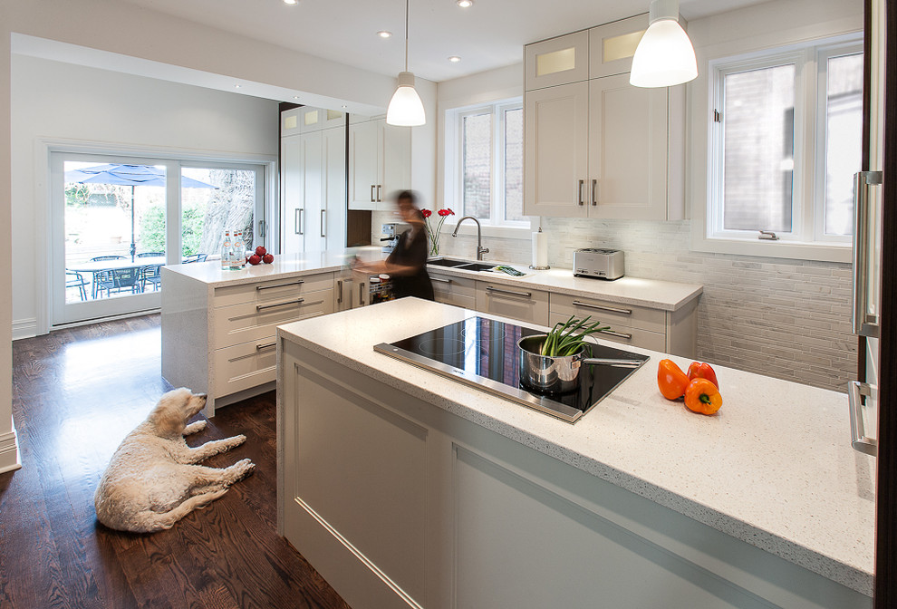 Design ideas for a contemporary galley open plan kitchen in Toronto with a double-bowl sink, recessed-panel cabinets, white cabinets, limestone benchtops, white splashback, terra-cotta splashback, stainless steel appliances, medium hardwood floors and multiple islands.