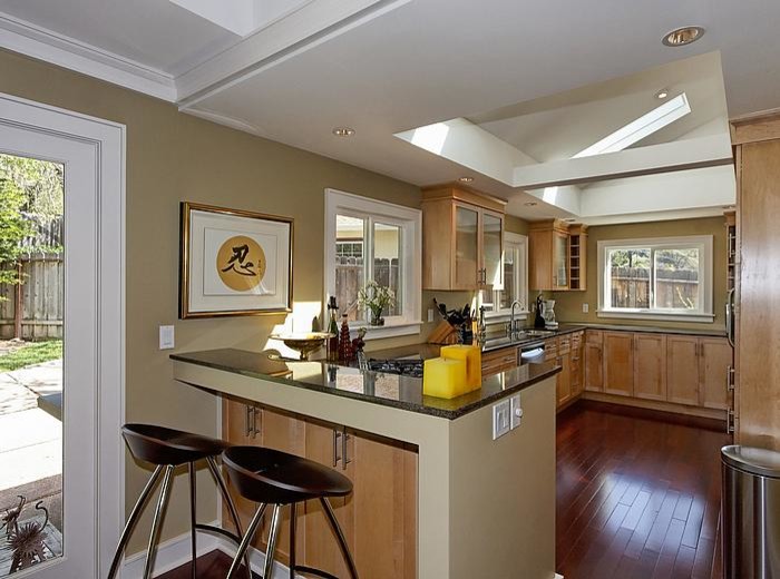 This is an example of a mid-sized u-shaped open plan kitchen in San Francisco with an undermount sink, shaker cabinets, light wood cabinets, granite benchtops, stainless steel appliances, dark hardwood floors, a peninsula and multi-coloured benchtop.