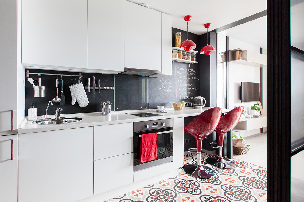 Small scandinavian single-wall open plan kitchen in Moscow with a drop-in sink, flat-panel cabinets, white cabinets, solid surface benchtops, black splashback, glass sheet splashback, stainless steel appliances, grey benchtop, porcelain floors, no island and multi-coloured floor.