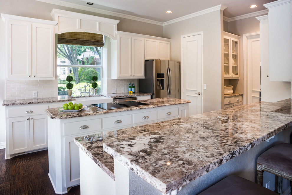 This is an example of a mid-sized country galley separate kitchen in Dallas with a farmhouse sink, shaker cabinets, white cabinets, granite benchtops, white splashback, stone tile splashback, stainless steel appliances, dark hardwood floors, multiple islands and brown floor.