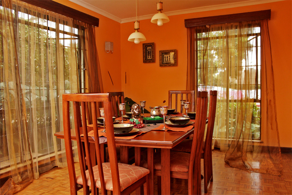 Esempio di una sala da pranzo aperta verso la cucina stile americano di medie dimensioni con pareti arancioni, pavimento in legno verniciato, camino ad angolo e cornice del camino in mattoni