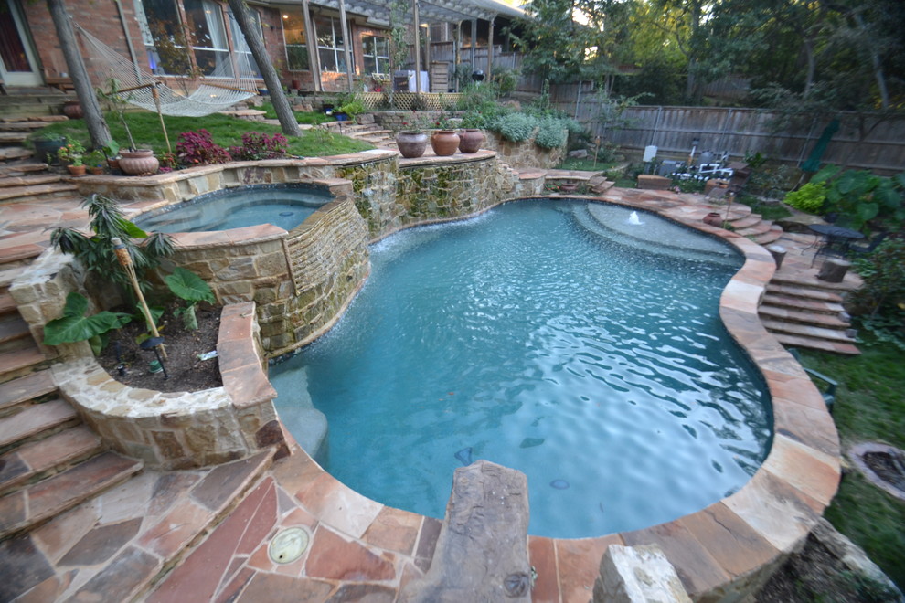 Large country backyard custom-shaped natural pool in Dallas with a water feature and natural stone pavers.