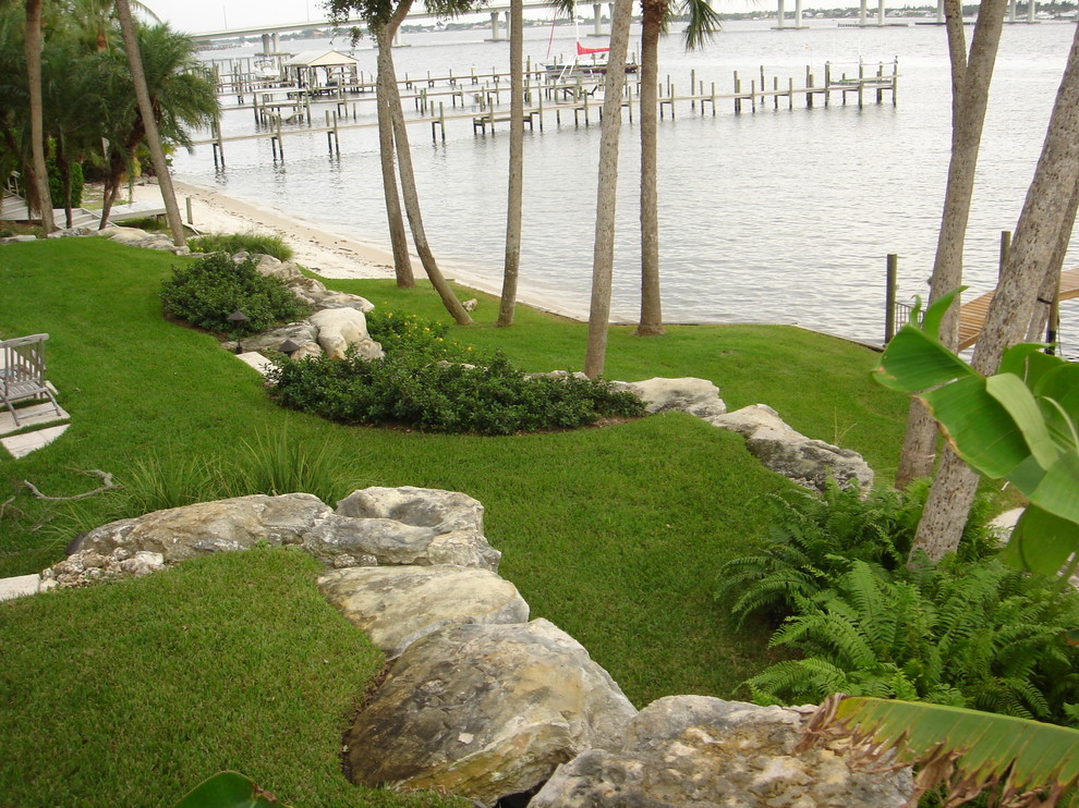 This is an example of a mid-sized tropical backyard partial sun formal garden for summer in Miami with a retaining wall and natural stone pavers.