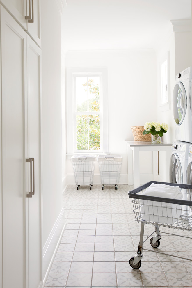 Inspiration for a transitional galley dedicated laundry room in Charleston with white cabinets, white walls, ceramic floors, a stacked washer and dryer, white floor, recessed-panel cabinets and grey benchtop.