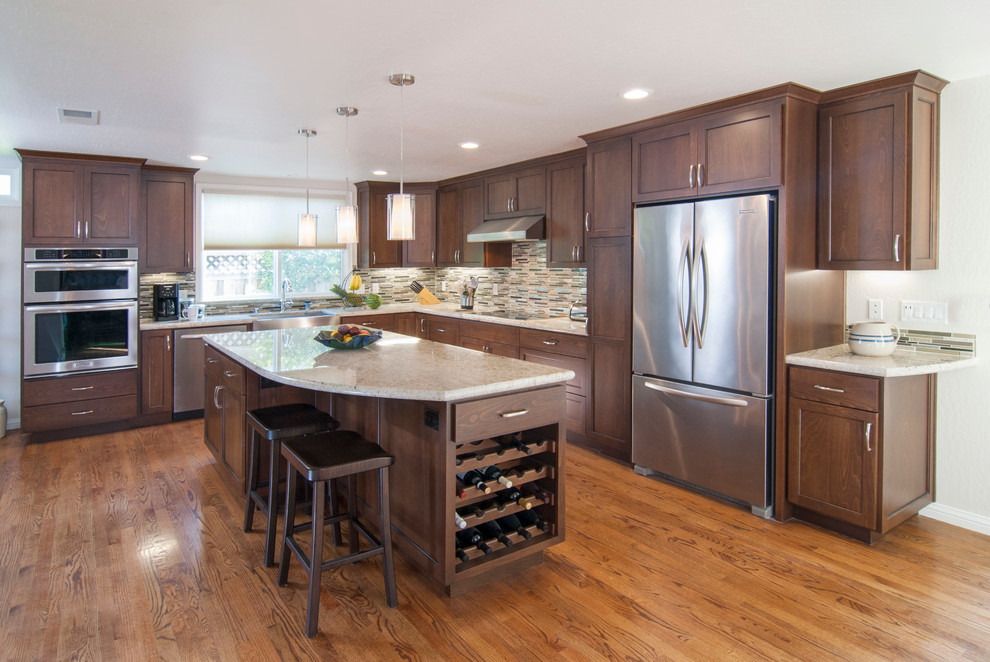 This is an example of a large contemporary l-shaped open plan kitchen in San Francisco with a farmhouse sink, shaker cabinets, brown cabinets, granite benchtops, beige splashback, glass tile splashback, stainless steel appliances, medium hardwood floors, with island and brown floor.