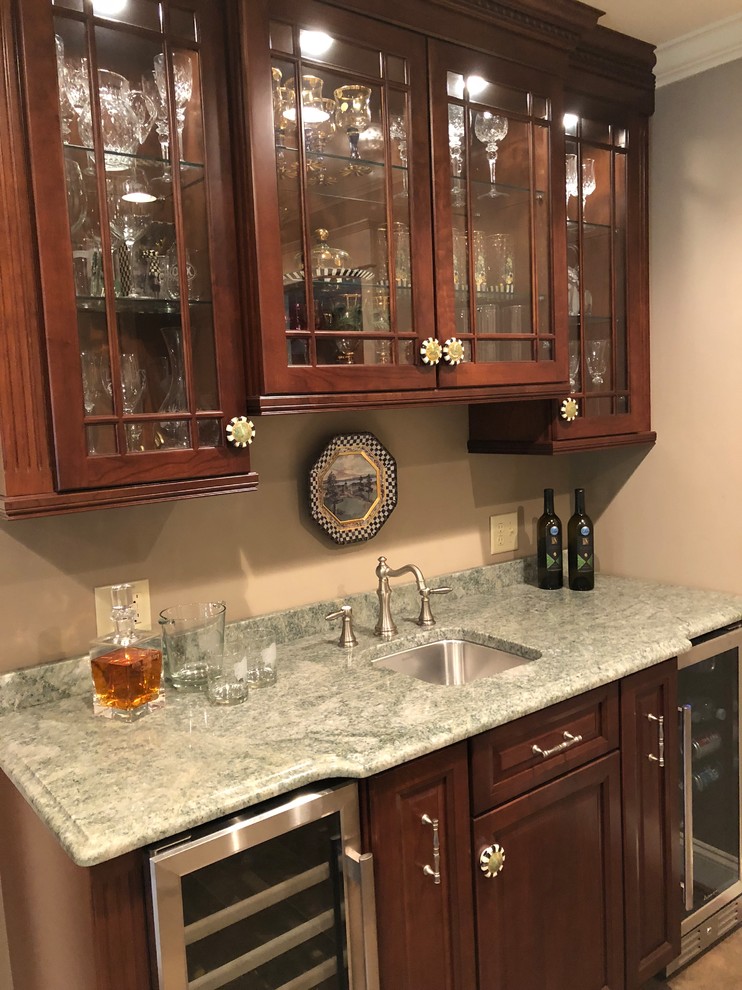 Photo of a traditional single-wall wet bar in New York with an undermount sink, raised-panel cabinets, medium wood cabinets, granite benchtops, ceramic floors, beige floor and green benchtop.